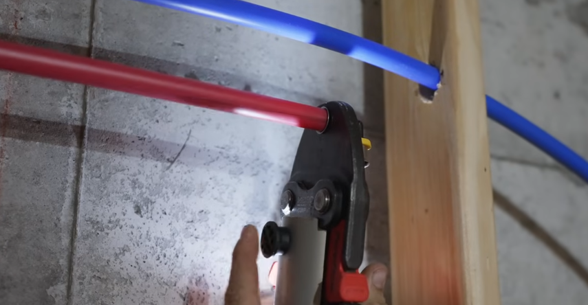 Cutting red and blue PEX supply tubing with a ratchet cutter during a repipe