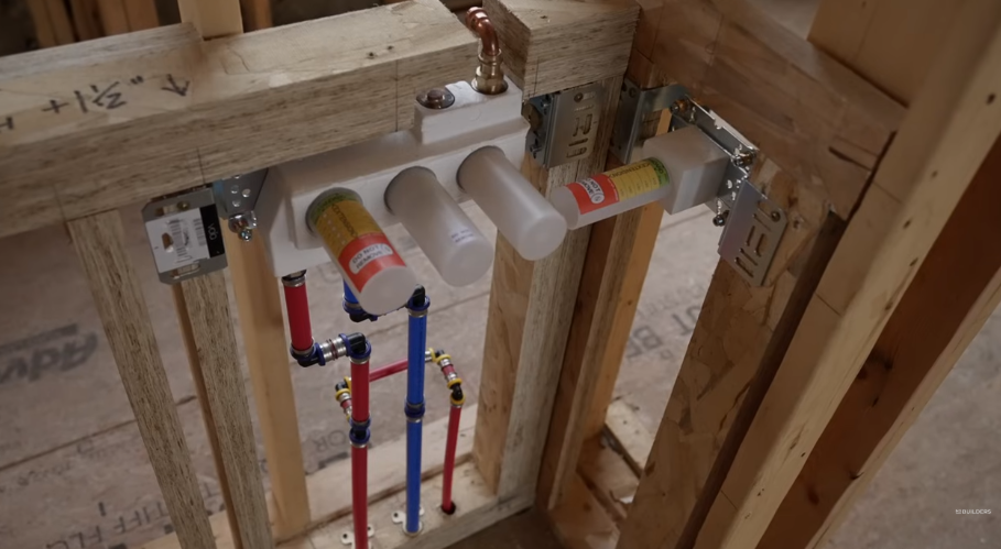PEX manifold with red and blue distribution lines mounted between wall studs