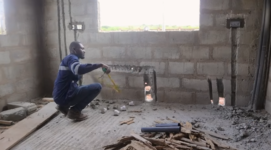 Measuring and marking pipe runs in a room stripped back to bare masonry