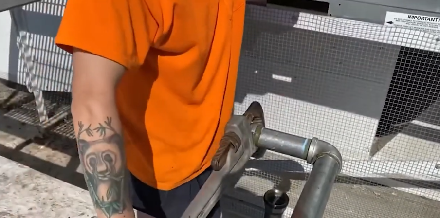 Technician working on galvanized pipework beside exterior equipment