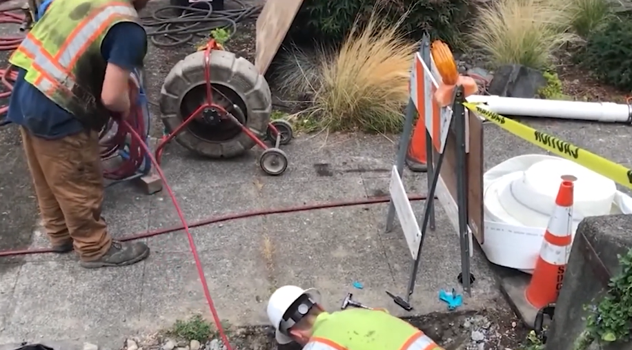 Crew running a cable machine into a sewer line from the street