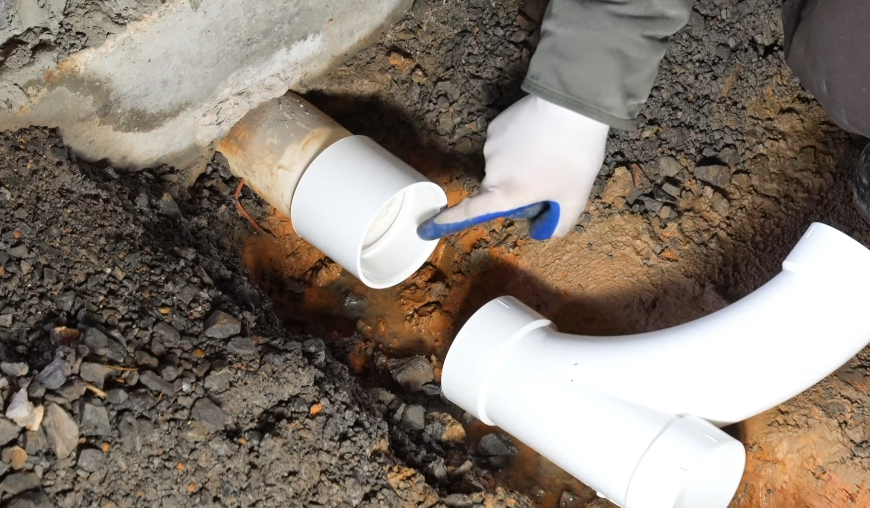 Replacing a section of drain line in an excavated trench through asphalt