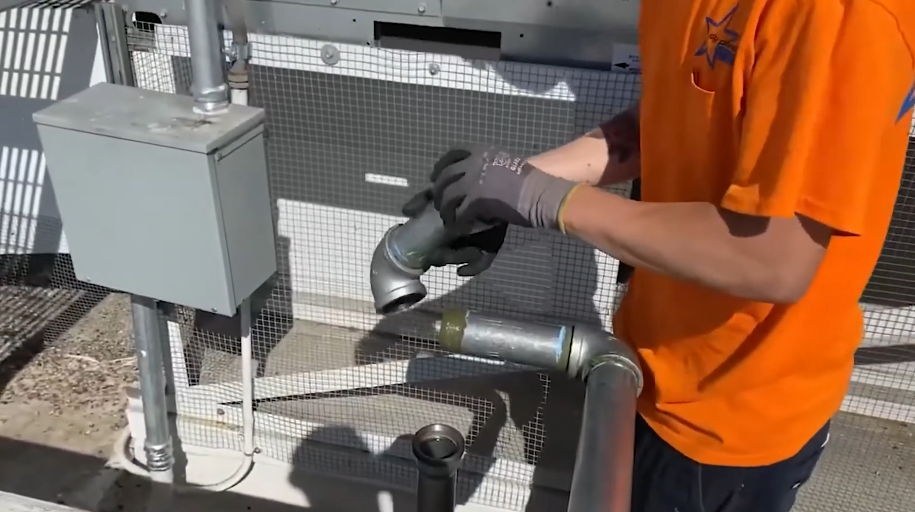 Technician servicing pipework at a commercial equipment enclosure
